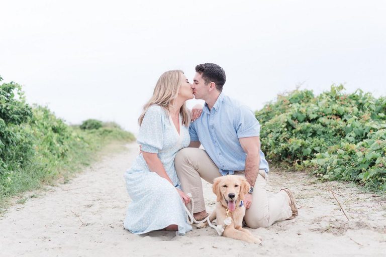 Engaged couple kneel down and kiss while holding their dog