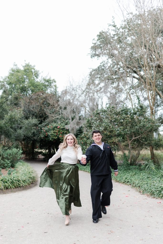 engaged couple run hand in hand through park