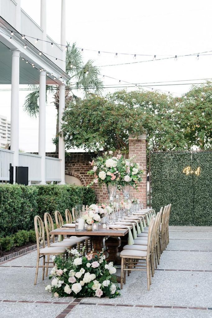 long farm table outside decorated with tall vases of roses and place settings