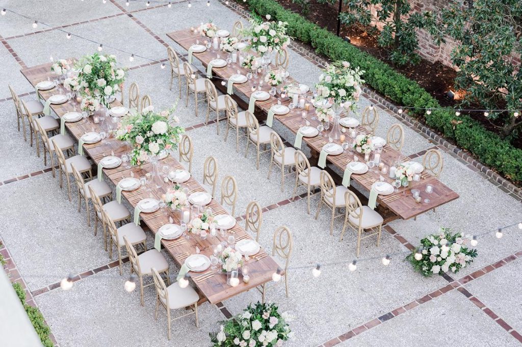 overview of two long wooden tables set for a wedding reception in a courtyard with string lights