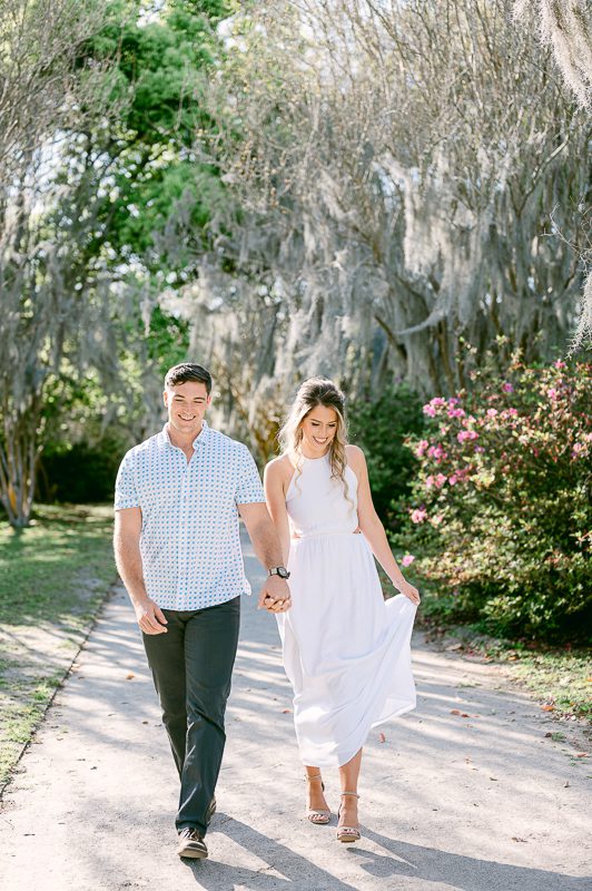 engaged couple walks hand in hand in park