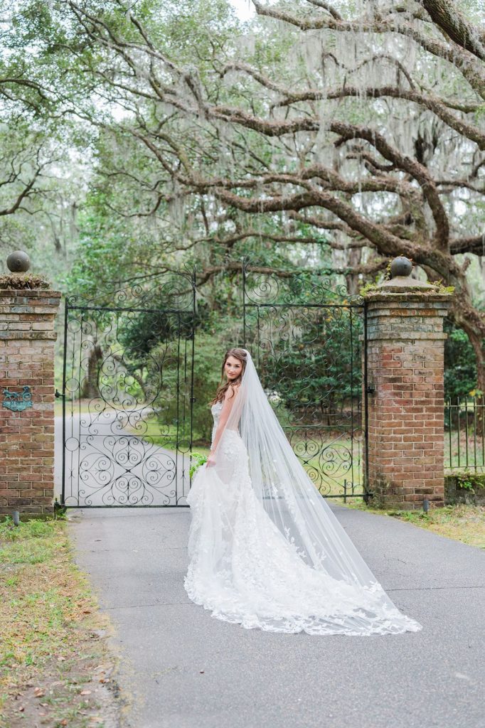 bride walking towards iron gate at Legare Waring House holding dress