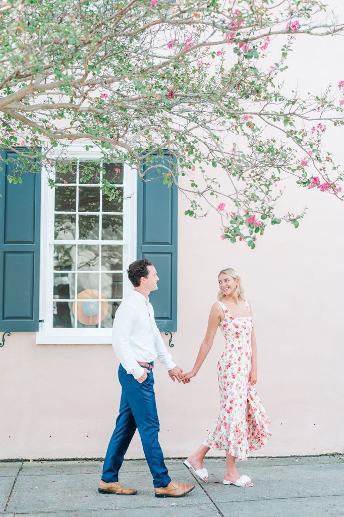 girl in floral dress leads fiancé down street by hand