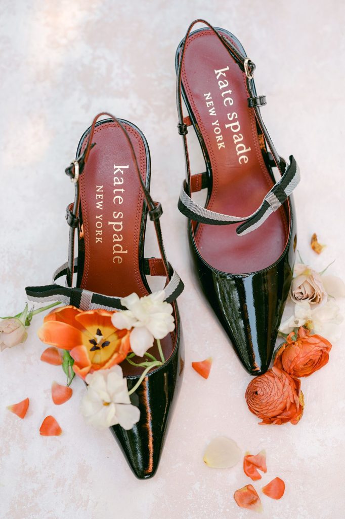 black patent leather Kate Spade shoes with flower petals laid around them