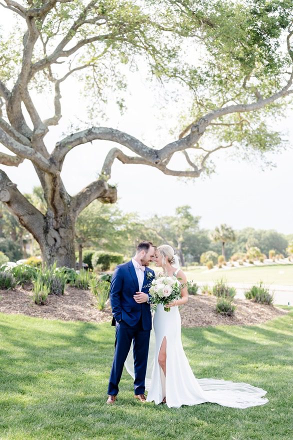 Newlyweds pose under oak tree next to golf course