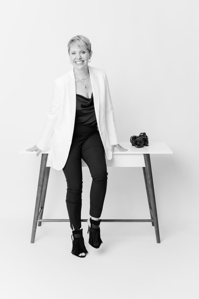 black and white photo of Photographer in white jacket sitting on edge of desk