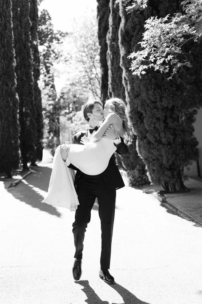 groom carries bride down alley with cypress trees