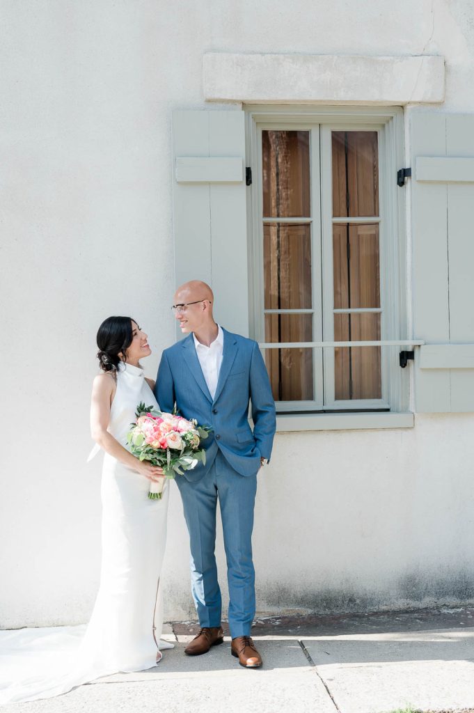 newlywed couple standing in front of pale green shutters of a house