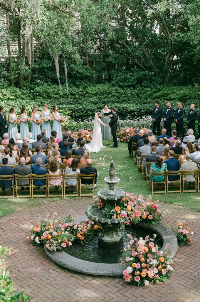 wedding ceremony in garden with water fountain decorated with pink and orange florals