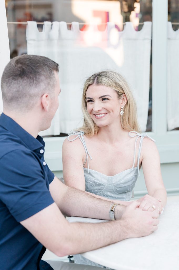 engaged girl looks lovingly at fiancé while holding hands at a table