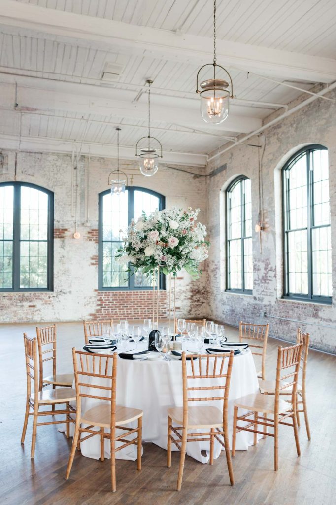 wedding reception set up with wood chairs, black napkins, and raised floral display
