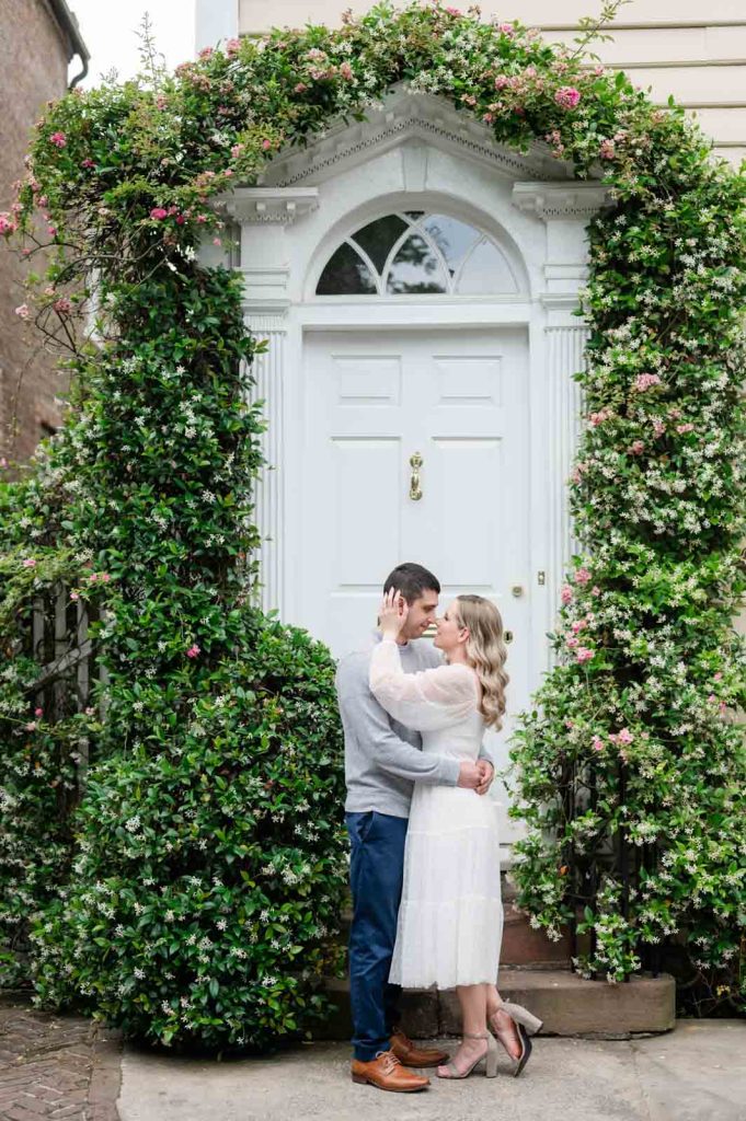 couple almost kisses in front of door with jasmine growing around it