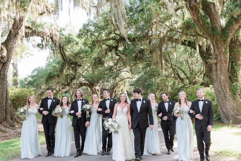 Bride and groom along with wedding party stroll under oak trees at Magnolia Plantation