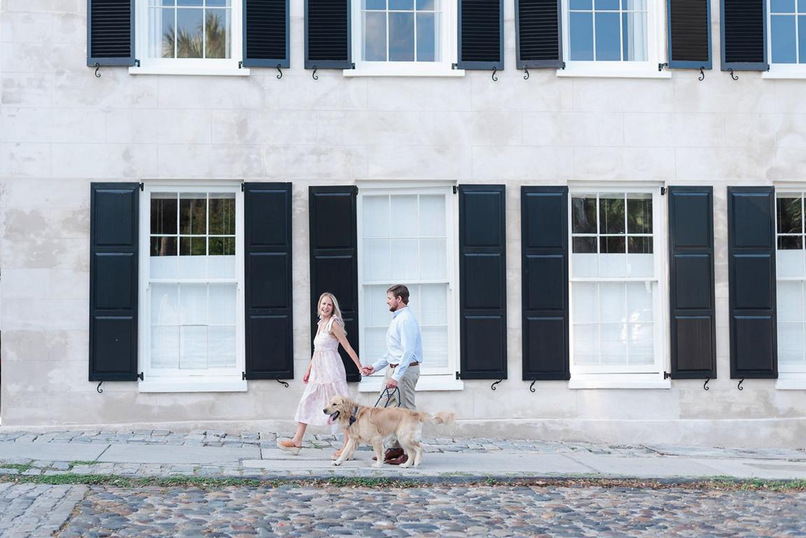 couple walking hand in hand on cobblestone street with their dog on a leash