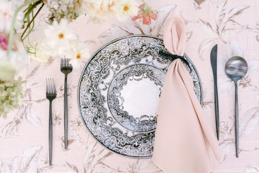table setting of black and white china and black silverware with pink napkin