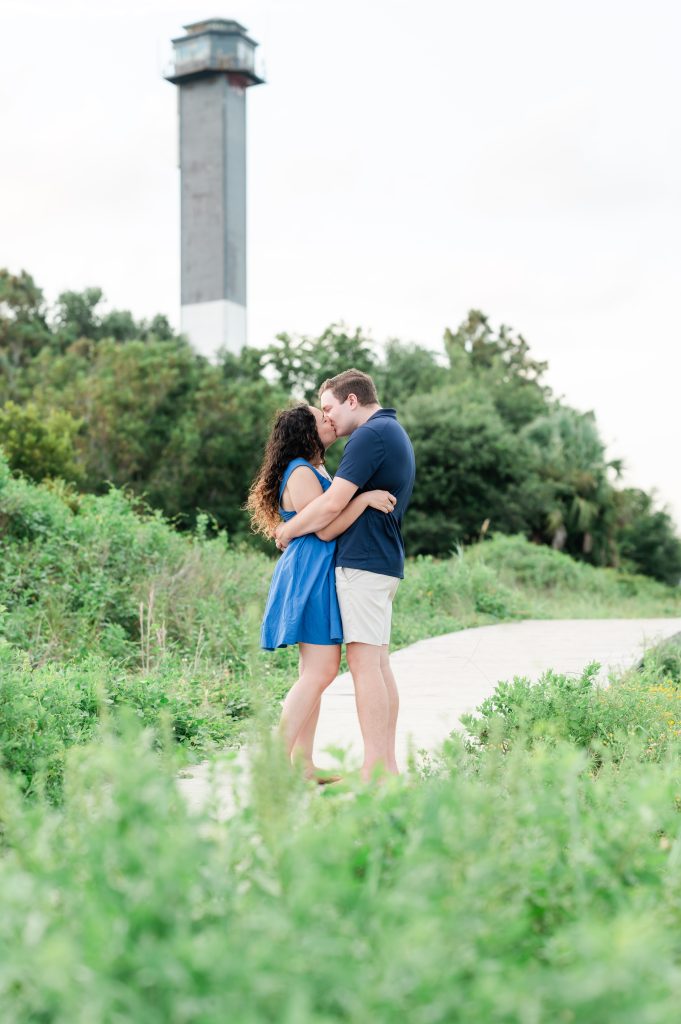 couple kiss and embrace in front of Sullivan Island lighthouse.