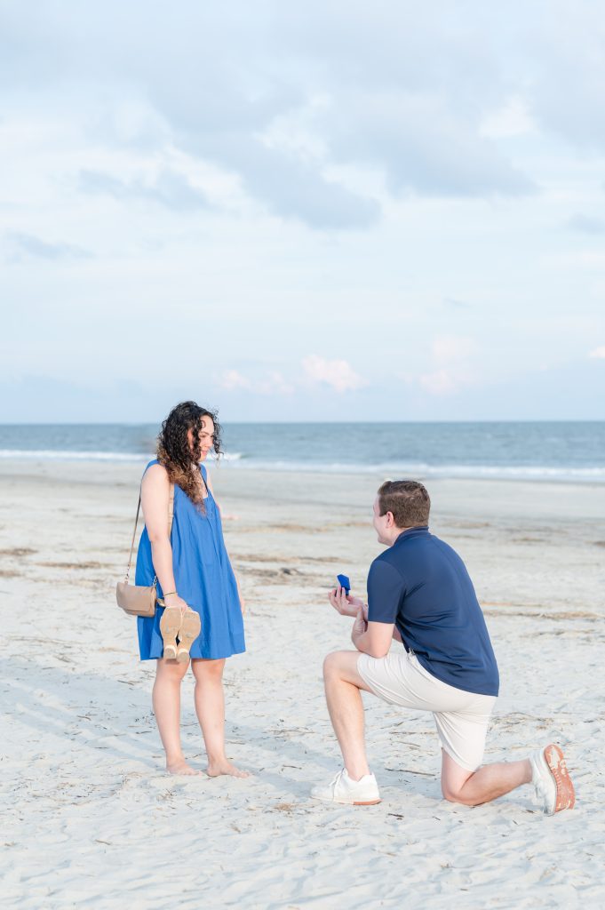 guy on bended knee in sand while proposing to girlfriend