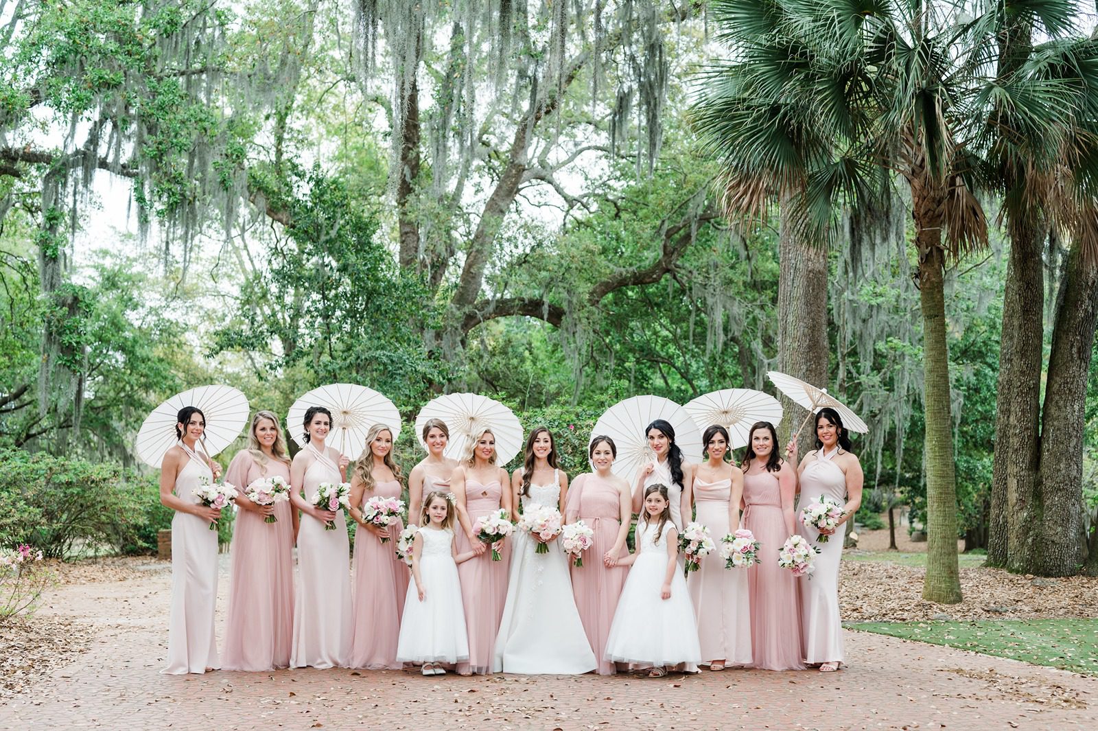 bride with large bridal party in blush dresses holding parasols