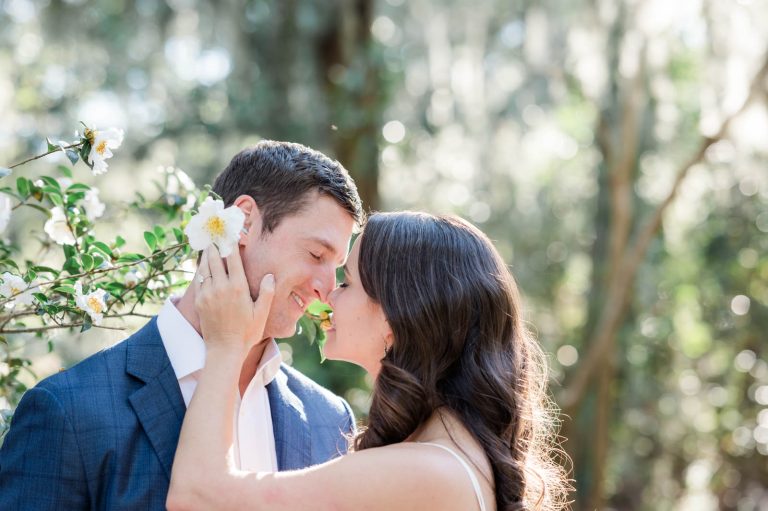 engaged couple lean in for a kiss while standing in camellia bush