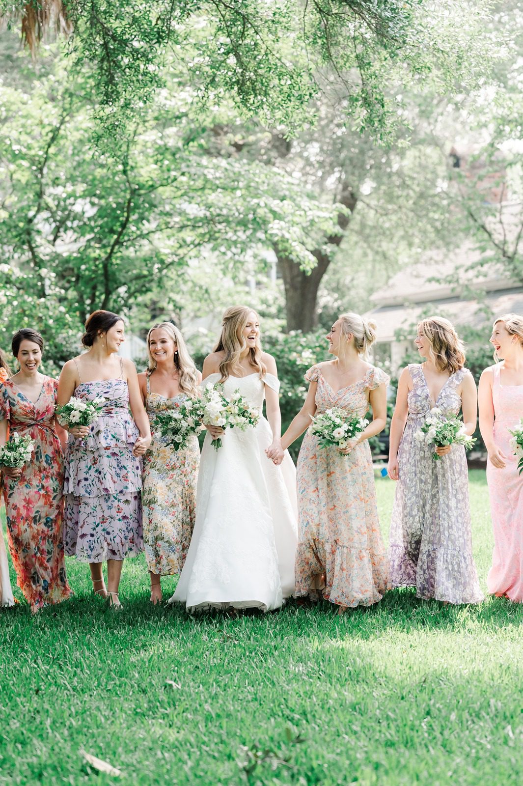 Bride and bridesmaids in different floral dresses walk together laughing