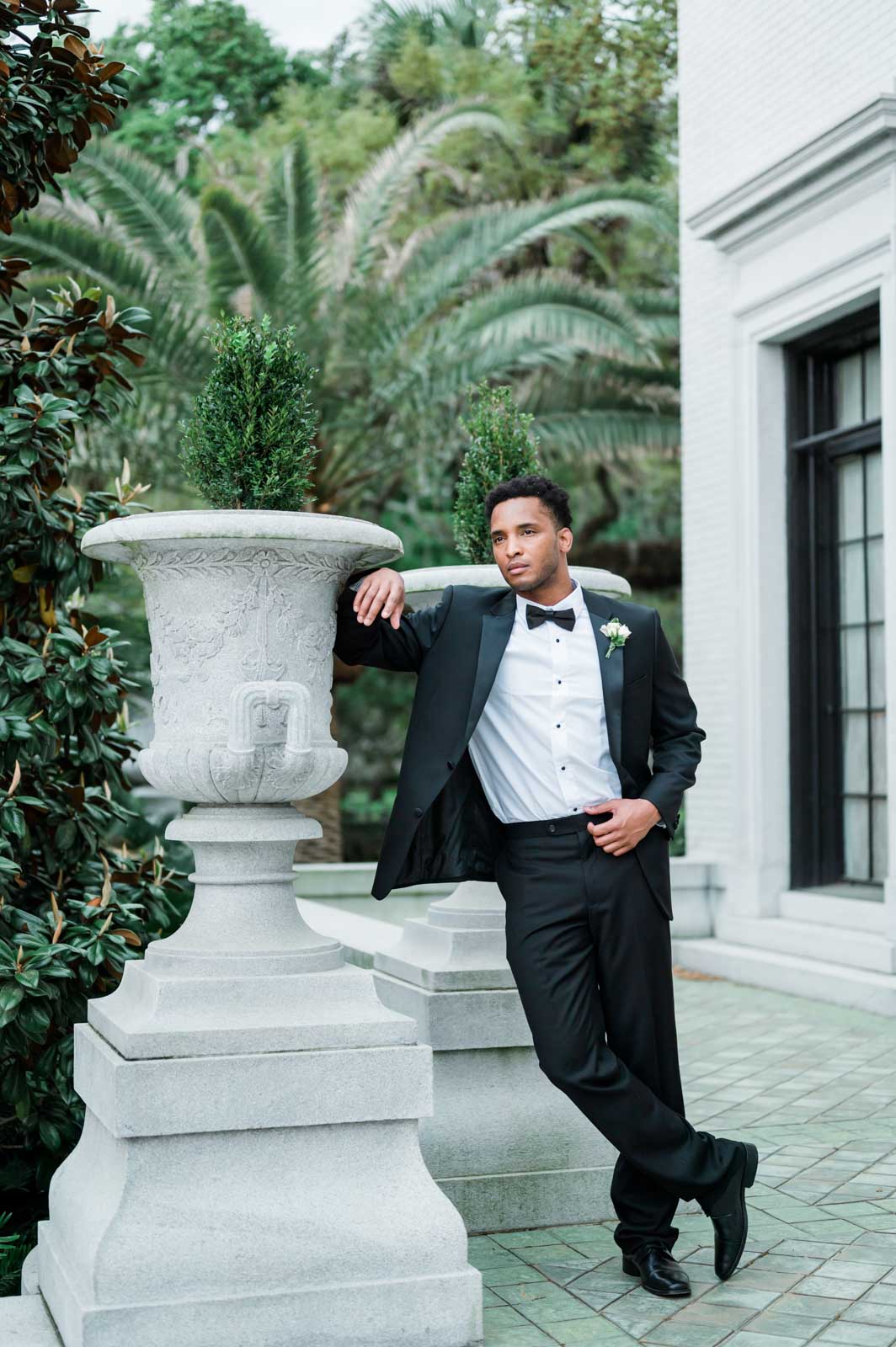 black groomsman in black tuxedo leaning against planter