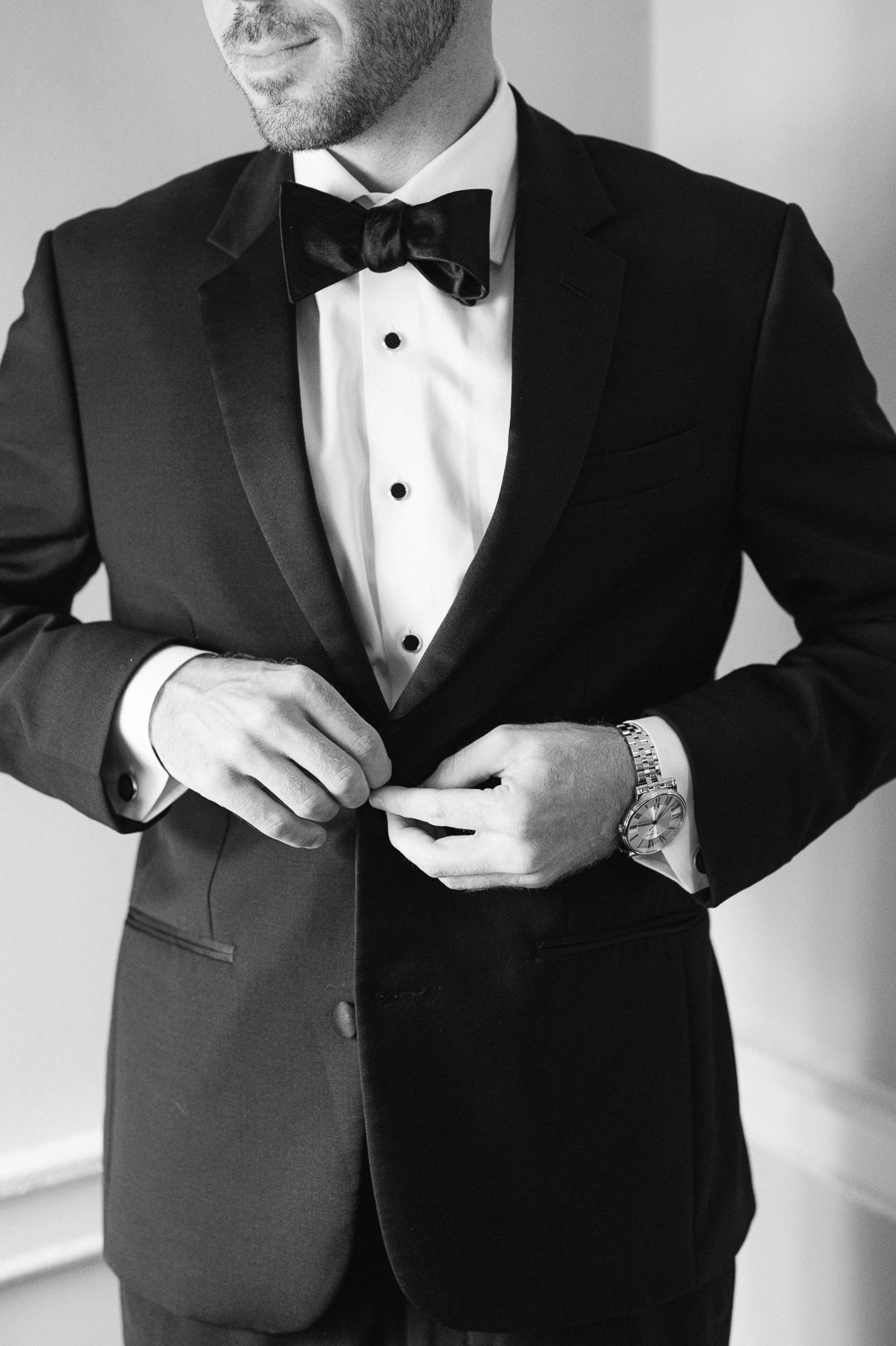 groom buttoning black tuxedo jacket