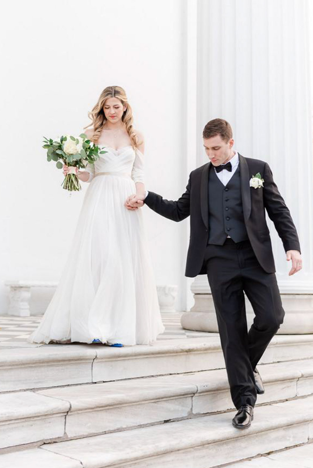 groom leading bride down white marble stairs