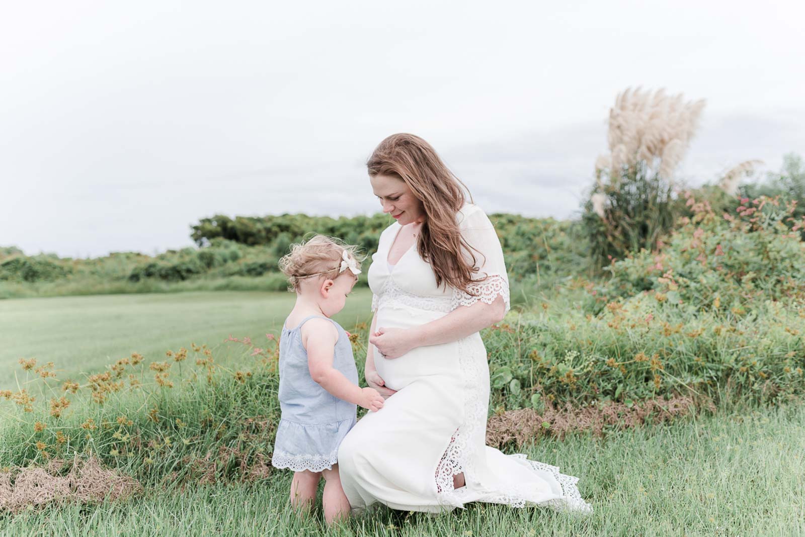 pregnant woman kneels to look at toddler