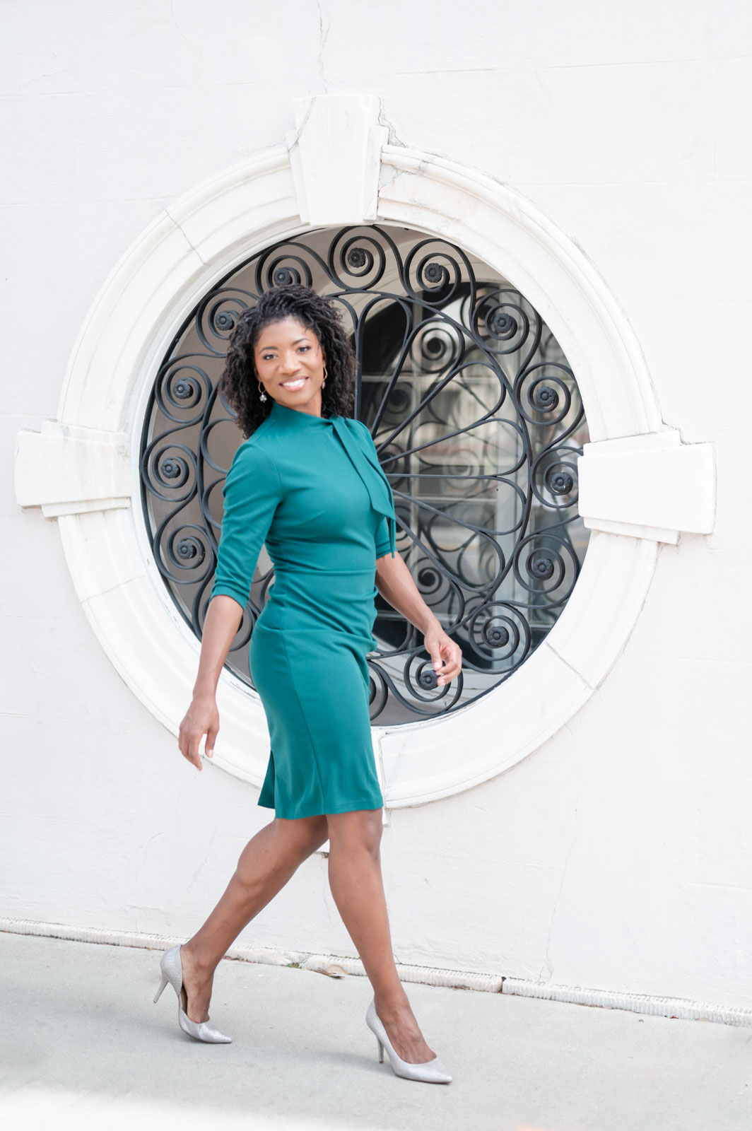 black woman in green dress walks confidently in front of circular window