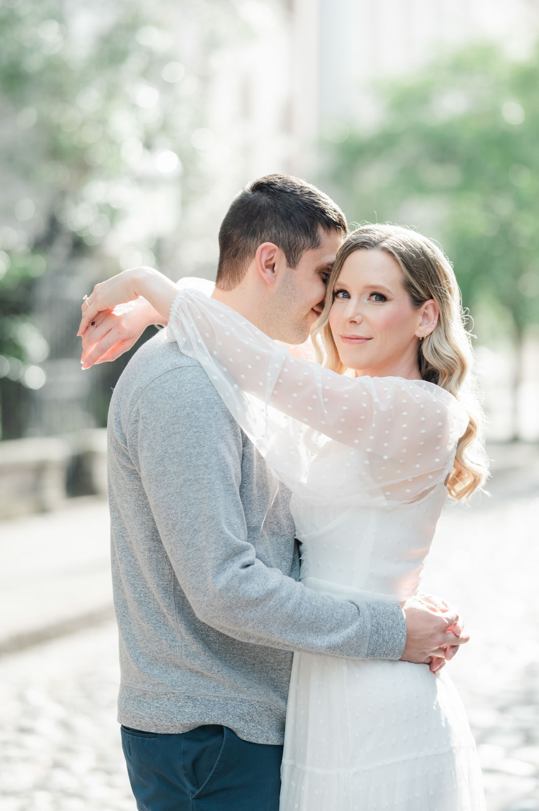 engaged young blonde woman drapes arms over fiancé's shoulder