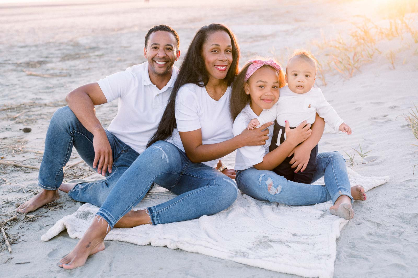 young family sits on blanket at beach during sunset