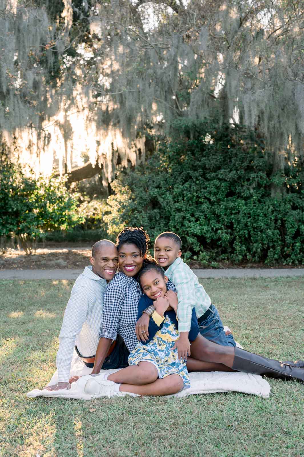 family sits on blanket at park with sun behind them